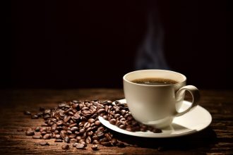 Eine dampfende Tasse Kaffe mit Kaffeebohnen